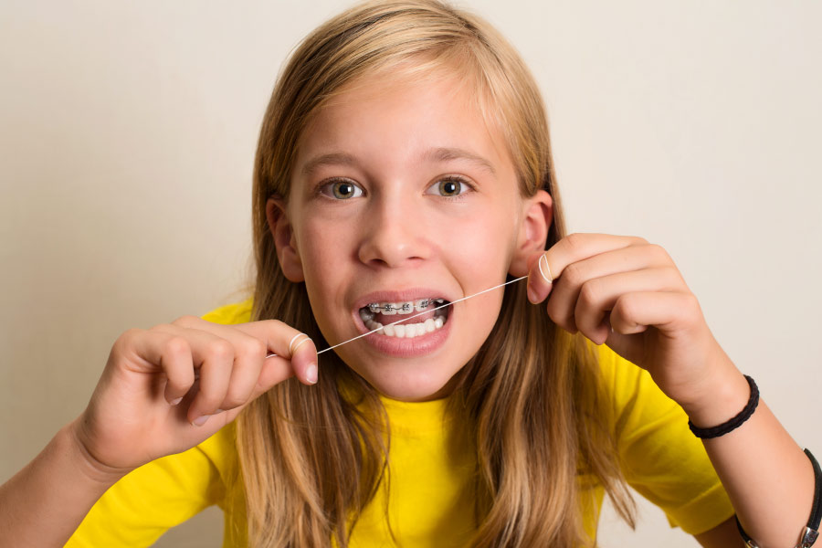 Teenage girl with long blond hair & braces flossing her teeth