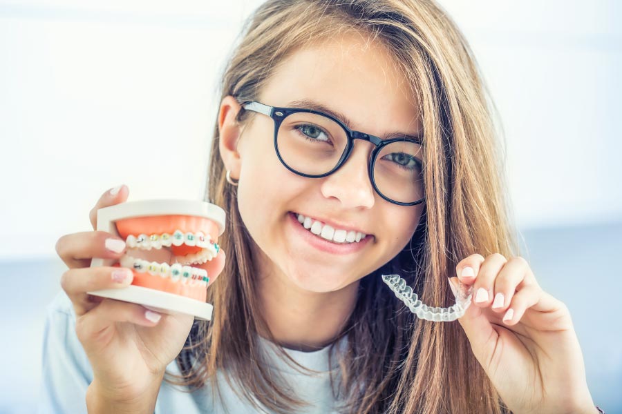 Smiling teen holding a model of teeth with braces and a clear retainer.
