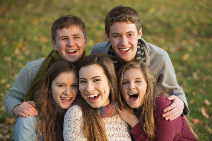 Coed group of teens smiling outside, some wearing braces